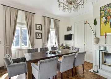 Elegantes Esszimmer mit Holztisch, Samtstühlen, Kronleuchter und Kamin.