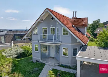 Freistehendes Einfamilienhaus mit Satteldach, Balkon und Carport in grüner Umgebung.