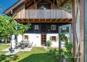 Traditionelles Bauernhaus mit weißer Fassade, Holzbalkonen und einem gemütlichen Gartenbereich mit Sitzgelegenheiten.