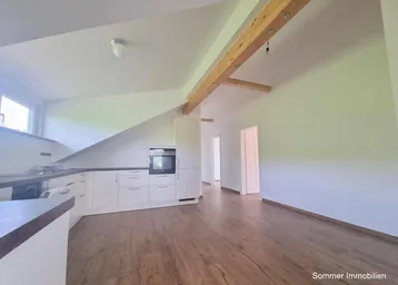 Moderne Küche mit weißen Schränken, Holzboden und sichtbarem Deckenbalken unter Dachschräge.