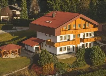 Traditionelles Haus mit rotem Dach, Holzbalkonen und einem Gartenpavillon in grüner Umgebung.