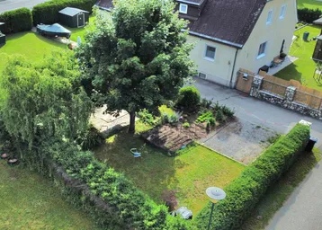 Luftaufnahme eines Hauses mit gepflegtem Garten, Bäumen und einer Zufahrt.