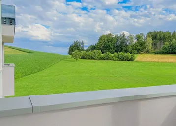 Blick von einem Balkon auf weite grüne Felder und eine hügelige Landschaft unter bewölktem Himmel.