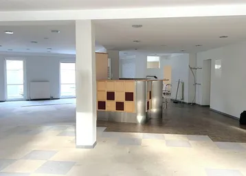 Großer, offener Raum mit einer Bar, kariertem Bodenbelag und mehreren Fenstern, der renovierungsbedürftig ist.