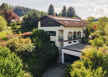 Ansicht des Hauses mit Balkonen, umgeben von üppiger Vegetation und Bäumen.