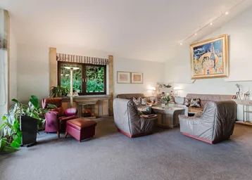 Großzügiges Wohnzimmer mit Teppichboden, Kamin und Blick in den Garten.