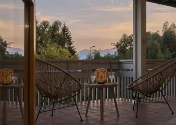 Gemütlicher Balkon mit Korbmöbeln und stimmungsvoller Beleuchtung bei Sonnenuntergang.