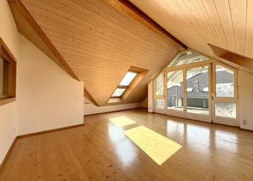 Helles Dachgeschosszimmer mit Holzbalkendecke, Parkettboden und großen Fenstern für viel Tageslicht.