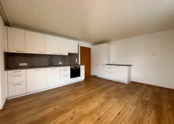 Moderne Einbauküche mit weißen Schränken, dunkler Arbeitsplatte und Holzfußboden in einem leeren Raum.