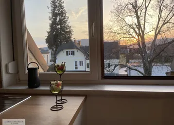 Blick aus der Küche bei Sonnenuntergang mit ländlicher Umgebung und einem Haus im Hintergrund.