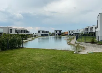 Wohngebiet mit einem zentralen See, umgeben von modernen Häusern und gepflegten Rasenflächen.