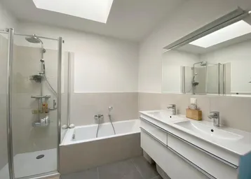 Modernes Badezimmer mit Badewanne, Duschkabine, Doppelwaschbecken und Oberlicht für viel Tageslicht.