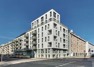 Modernes Eckgebäude mit mehreren Etagen und Balkonen an einer städtischen Kreuzung.