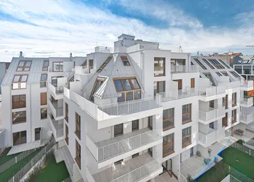 Modernes Wohngebäude mit vielen Balkonen und Dachterrassen unter blauem Himmel.