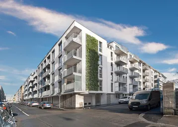 Modernes Wohngebäude mit weißer Fassade, Balkonen und vertikaler Begrünung unter blauem Himmel.