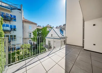 Heller Balkon mit Fliesenboden und Blick auf begrünte Innenhöfe und umliegende Gebäude.