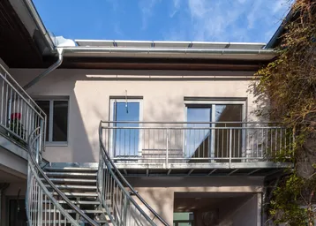 Außenansicht des Gebäudes mit Metalltreppe und Balkonen unter blauem Himmel und Solaranlage auf dem Dach.