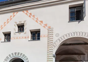 Fassade eines historischen Gebäudes mit traditionellen Mustern und Fenstern unter blauem Himmel.