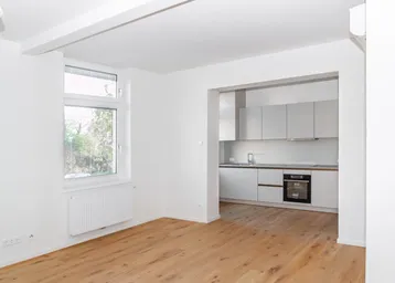 Heller Wohnbereich mit Holzfußboden und Zugang zur modernen Einbauküche.