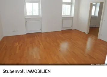 Helles, leeres Wohnzimmer mit schönem Parkettboden und zwei Fenstern, die viel Tageslicht hereinlassen.