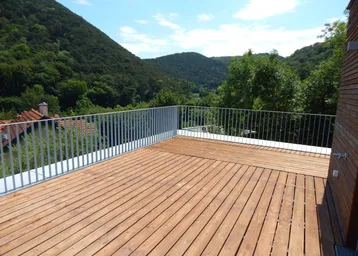Große Holzterrasse mit modernem Geländer und weitem Blick auf die umliegende grüne Hügellandschaft.