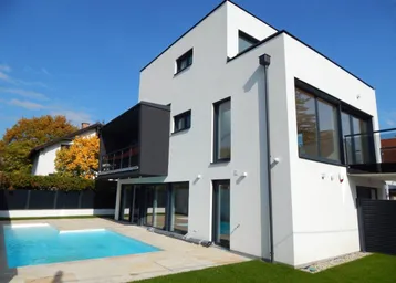 Modernes Einfamilienhaus mit klaren Linien, großem Pool und gepflegtem Gartenbereich unter blauem Himmel.