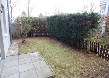 Kleiner privater Gartenbereich mit Rasenfläche, Hecke und gepflasterter Terrasse.