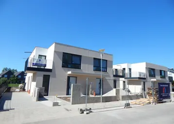 Moderne Doppelhaushälfte im Bau mit klaren Linien und Balkonen unter blauem Himmel.