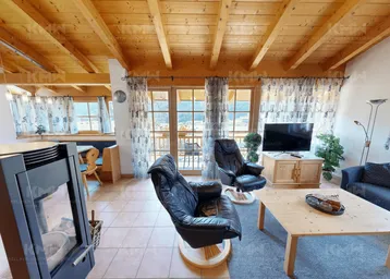 Gemütlicher Wohn-Essbereich im alpinen Stil mit Kamin, Holzbalkendecke und großen Fenstern mit Bergblick.