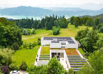 Moderne Villa mit Gründach und Solaranlagen, umgeben von Natur mit See- und Bergblick.