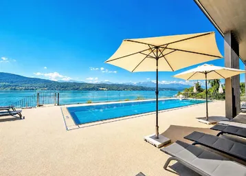 Großer Außenpoolbereich mit Liegestühlen, Sonnenschirmen und weitem Blick auf den See und die Berge.