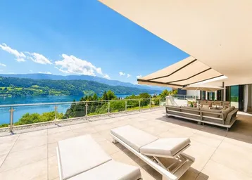 Geräumige Terrasse mit bequemen Lounge-Möbeln, Sonnenliegen und einem atemberaubenden Blick auf den See und die Berge.