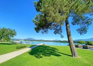 Idyllischer Blick auf den Faakersee mit grünen Ufern und majestätischen Bergen im Hintergrund.