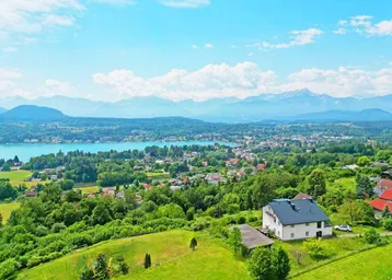 Panoramablick auf den See, die Berge und die umliegende grüne Landschaft mit einem Einfamilienhaus.