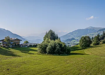 Panoramablick auf ein traditionelles Haus in einer grünen Berglandschaft unter blauem Himmel.
