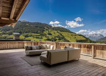 Großzügige Holzterrasse mit bequemen Loungemöbeln und spektakulärem Blick auf die grüne Berglandschaft.