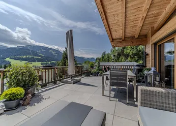 Große Terrasse mit Essbereich, Liegestühlen und beeindruckendem Bergblick unter einem Holzdach.