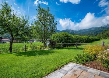 Grüner Gartenbereich mit Rasenfläche, Obstbäumen und Blick auf die umliegende Berglandschaft.