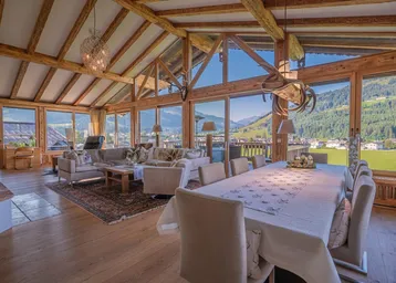 Geräumiger Wohn- und Essbereich mit hohen Decken, Holzbalken und Panoramablick auf die Berge.