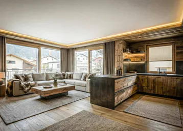 Geräumiger offener Wohn- und Essbereich mit moderner Küche, Holzelementen und großen Fenstern mit Bergblick.