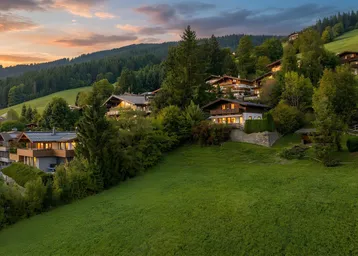 Panoramablick auf mehrere Häuser in einer grünen Hügellandschaft bei Sonnenuntergang.