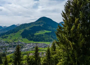 Panoramablick auf ein malerisches Tal mit einer Stadt, umgeben von grünen Hügeln und majestätischen Bergen.