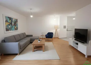 Helles Wohnzimmer mit modernem Sofa, Holztisch und offener Küchenzeile im Hintergrund.