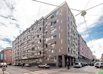 Großes Wohngebäude an einer Straßenecke mit vielen Fenstern und urbaner Umgebung.