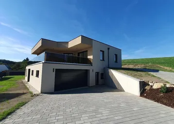 Moderne Neubauvilla mit integrierter Doppelgarage, gepflasterter Auffahrt und großem Balkon mit Glasgeländer.