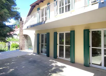 Große gepflasterte Terrasse vor dem Haus mit grünen Fensterläden und Balkon im Obergeschoss.