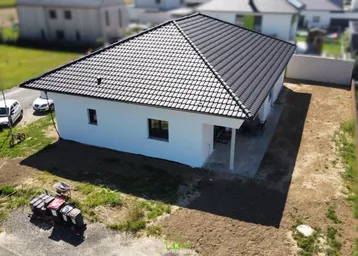 Neubau-Einfamilienhaus mit dunklem Ziegeldach und weißer Fassade in ländlicher Umgebung.