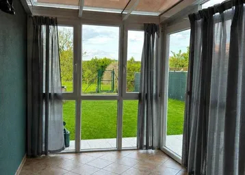 Heller Wintergarten mit Glasdach, Fliesenboden und direktem Zugang zum grünen Garten.