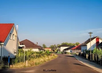 Blick auf eine ruhige Wohnstraße mit mehreren Einfamilienhäusern und gepflegten Gärten unter blauem Himmel.
