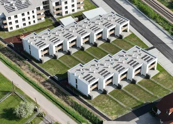Luftaufnahme einer modernen Wohnsiedlung mit Reihenhäusern und Photovoltaikanlagen auf den Dächern.